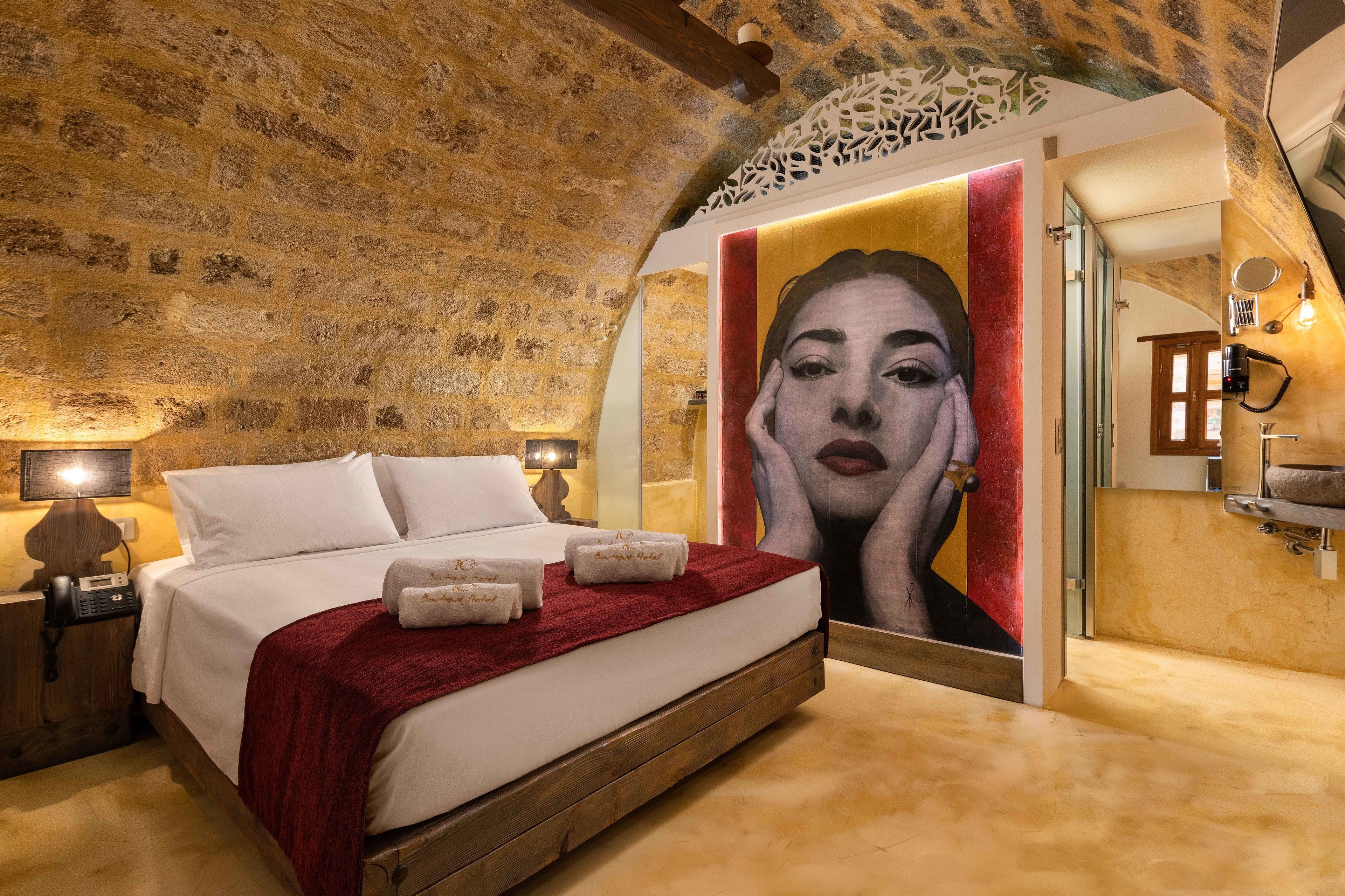 A bedroom with a stone ceiling, a bed with white linens, a red throw blanket, and a large painting on the wall.