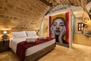 A bedroom with a stone ceiling, a bed with white linens, a red throw blanket, and a large painting on the wall.