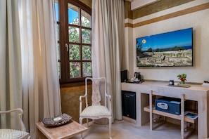 A room with a wooden desk, a chair, a television mounted on the wall, and a window with curtains.