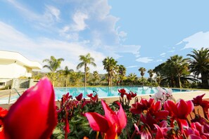 A pool area with palm trees and red flowers in the foreground.