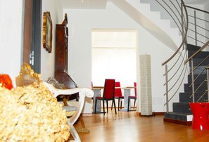 A spacious living area with a staircase, a dining table with red chairs, and a large window providing natural light.
