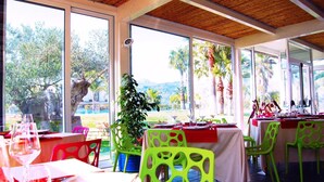 An outdoor dining area with tables and chairs, large windows, and a view of trees and hills.