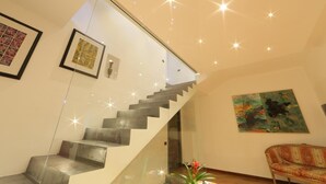 A modern staircase with glass railings, a framed abstract painting, and a colorful chair in a well-lit room.