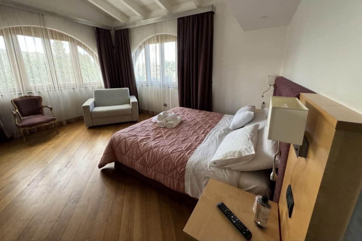 A hotel room with a large bed, a chair, a small table with a remote control, and a nightstand.