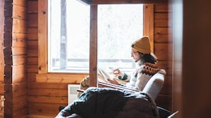 Une chambre confortable dans un chalet, avec un intérieur en bois, un lit recouvert d’une couverture à motifs et une fenêtre laissant entrer la lumière naturelle.