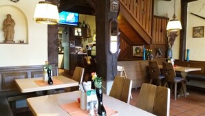 A restaurant interior with wooden tables and chairs, a stone statue, and a television on the wall. - Gasthof Stadtschänke (Grossbottwar)