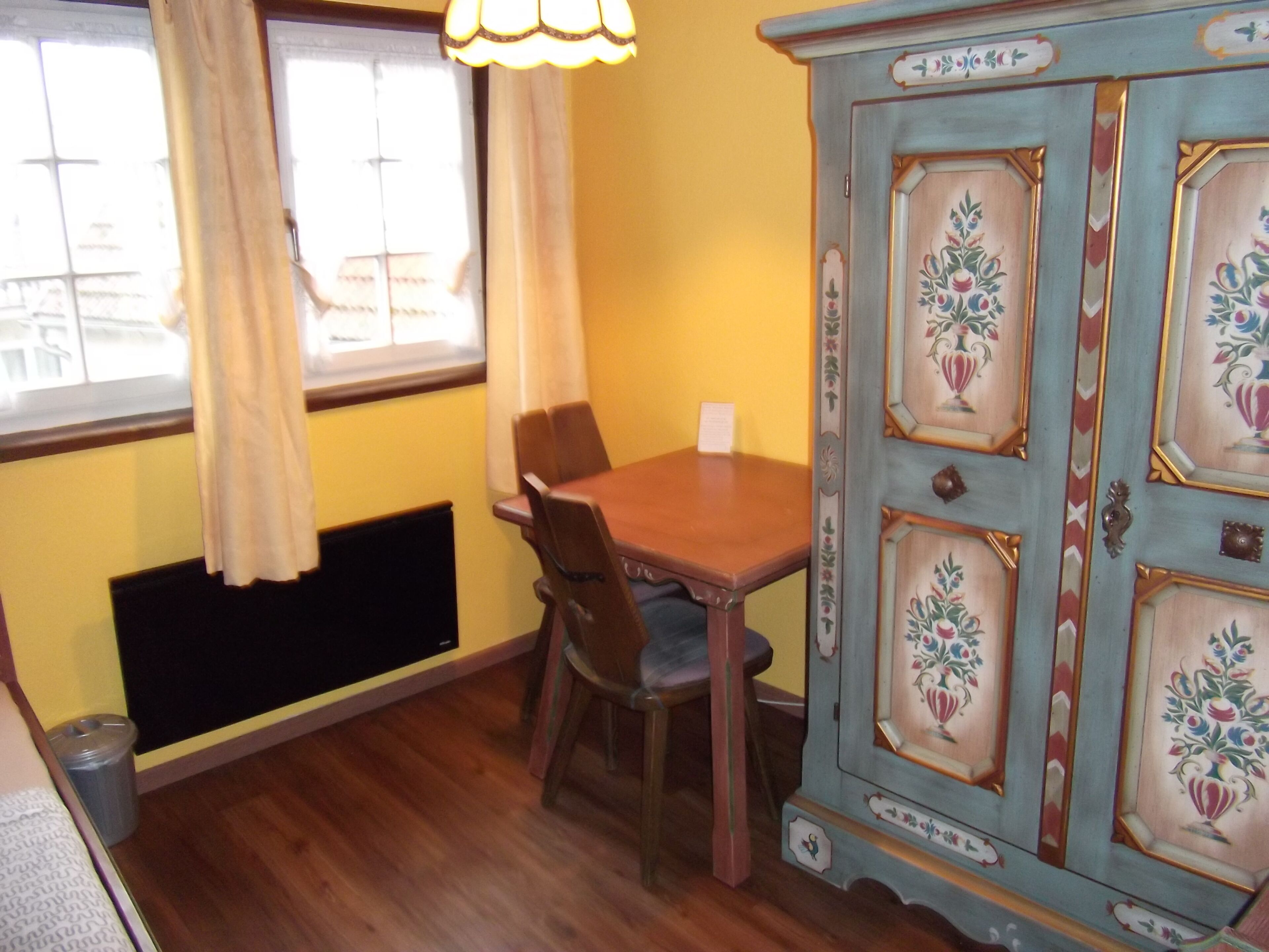Un coin repas avec une table et des chaises en bois, un buffet orné de motifs floraux et une fenêtre avec des rideaux.