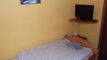 Ein kleines Zimmer mit einem Einzelbett, einem Fernseher auf einer Holzablage und einem Gemälde, das eine Küstenlandschaft zeigt.