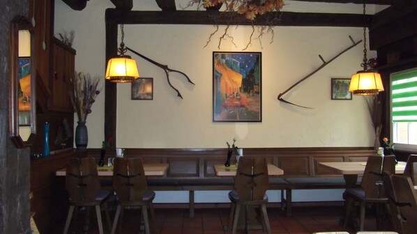 L’intérieur d’un restaurant avec des bancs et des tables en bois, des lampes suspendues et un tableau au mur.