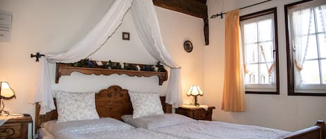 A bedroom with a wooden bed, a canopy, two bedside tables with lamps, and a window with curtains.