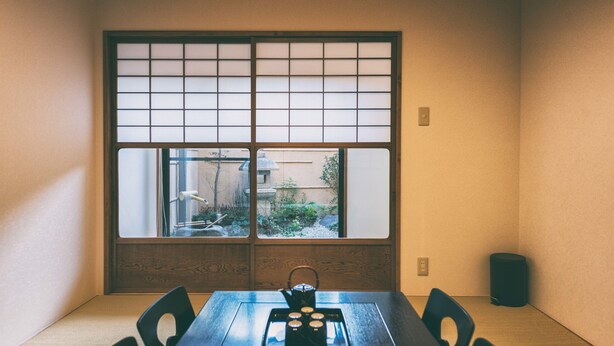 Une pièce traditionnelle japonaise avec un sol recouvert de tatamis, une petite table sur laquelle est disposé un service à thé et une fenêtre à panneaux coulissants de type shoji.