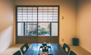 A traditional Japanese room with tatami flooring, a low table with a tea set, and a shoji screen window.