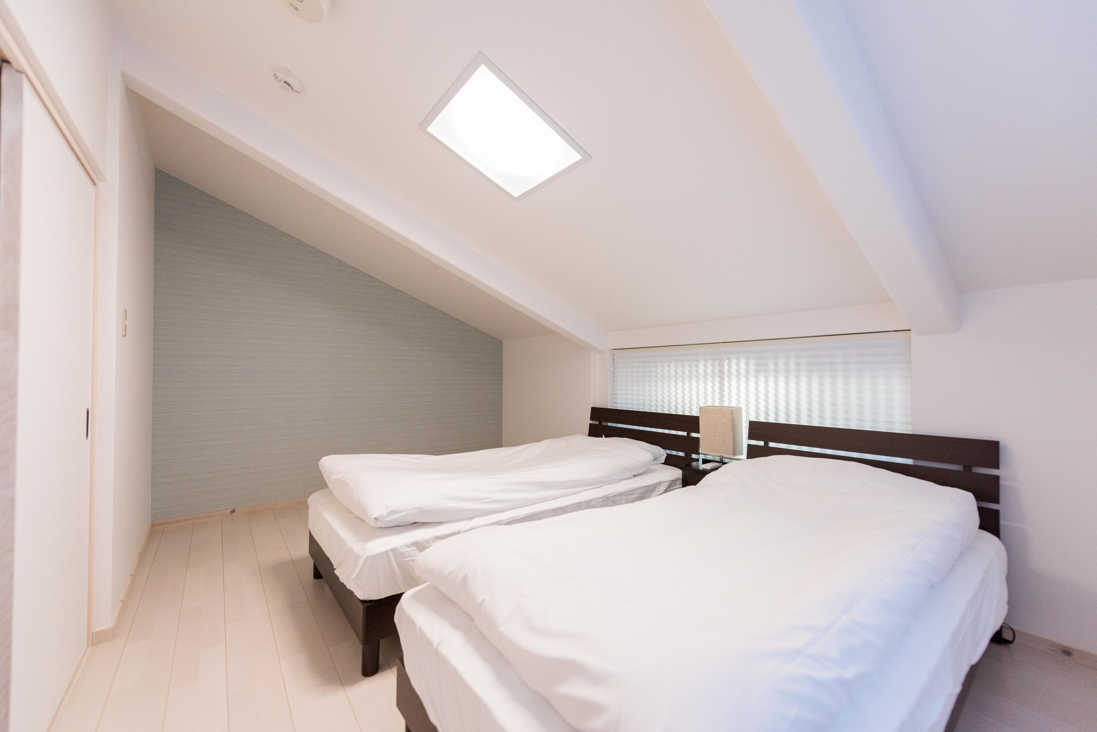 Ein Schlafzimmer mit zwei Betten, einem Oberlicht, einem Fenster mit Jalousien und Holzboden.