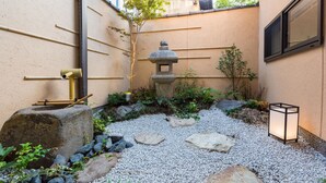 Un jardin agrémenté d’une lanterne en pierre, de bambous et d’un petit arbre.