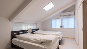 Une chambre avec deux lits, un puits de lumière, un appareil de climatisation et une fenêtre avec des stores.
