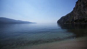 A calm lake with clear water, a sandy beach, and a rocky cliff. - Hotel e Appartamenti al Prà de la Fam (Tignale)