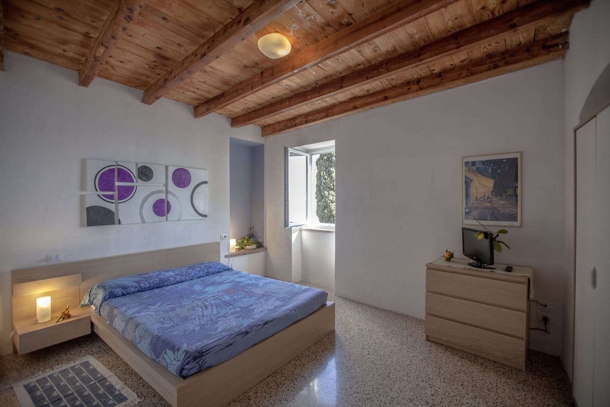 Un dormitorio con una cama, un tocador, un televisor y obras de arte en las paredes.
