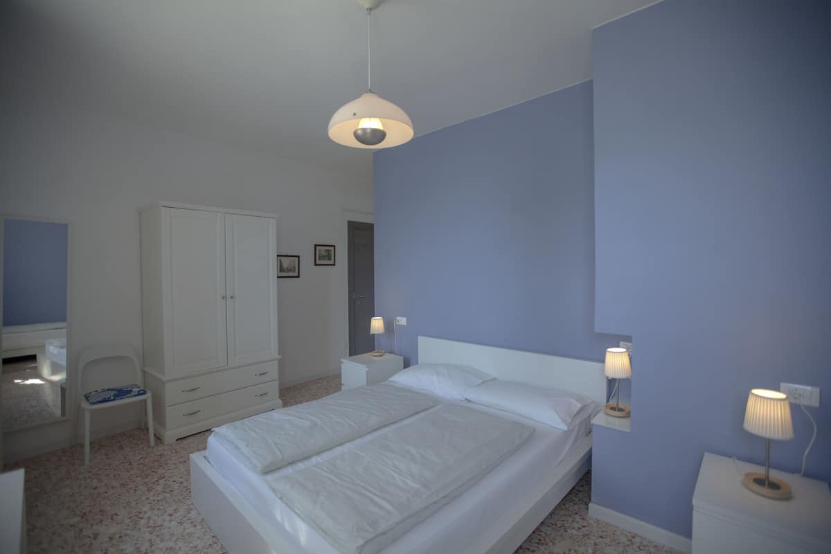 Un dormitorio con cama, armario, escritorio y dos lámparas de noche.