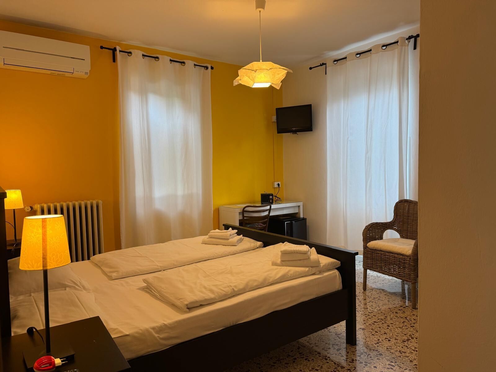 Une chambre d’hôtel équipée d’un lit, d’un bureau, d’une chaise, d’un climatiseur, d’une lampe et d’un téléviseur.