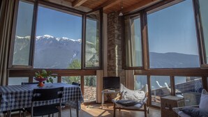 A room with wooden beams, large windows, a dining table with chairs, a sofa, and a view of snow-capped mountains. - Hotel e Appartamenti al Prà de la Fam (Tignale)