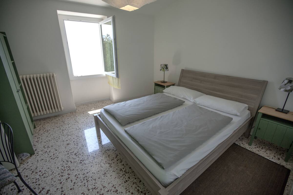 Un dormitorio con cama, mesita de noche, lámpara, radiador y ventana.