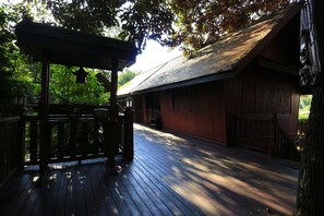 A wooden deck with a pergola, a building with a sloped roof, and a tree with a carved face. - Kawila126 Villa (Chiang Mai)