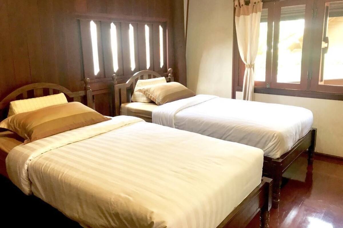 A room with two beds, wooden headboards, and a window with curtains.