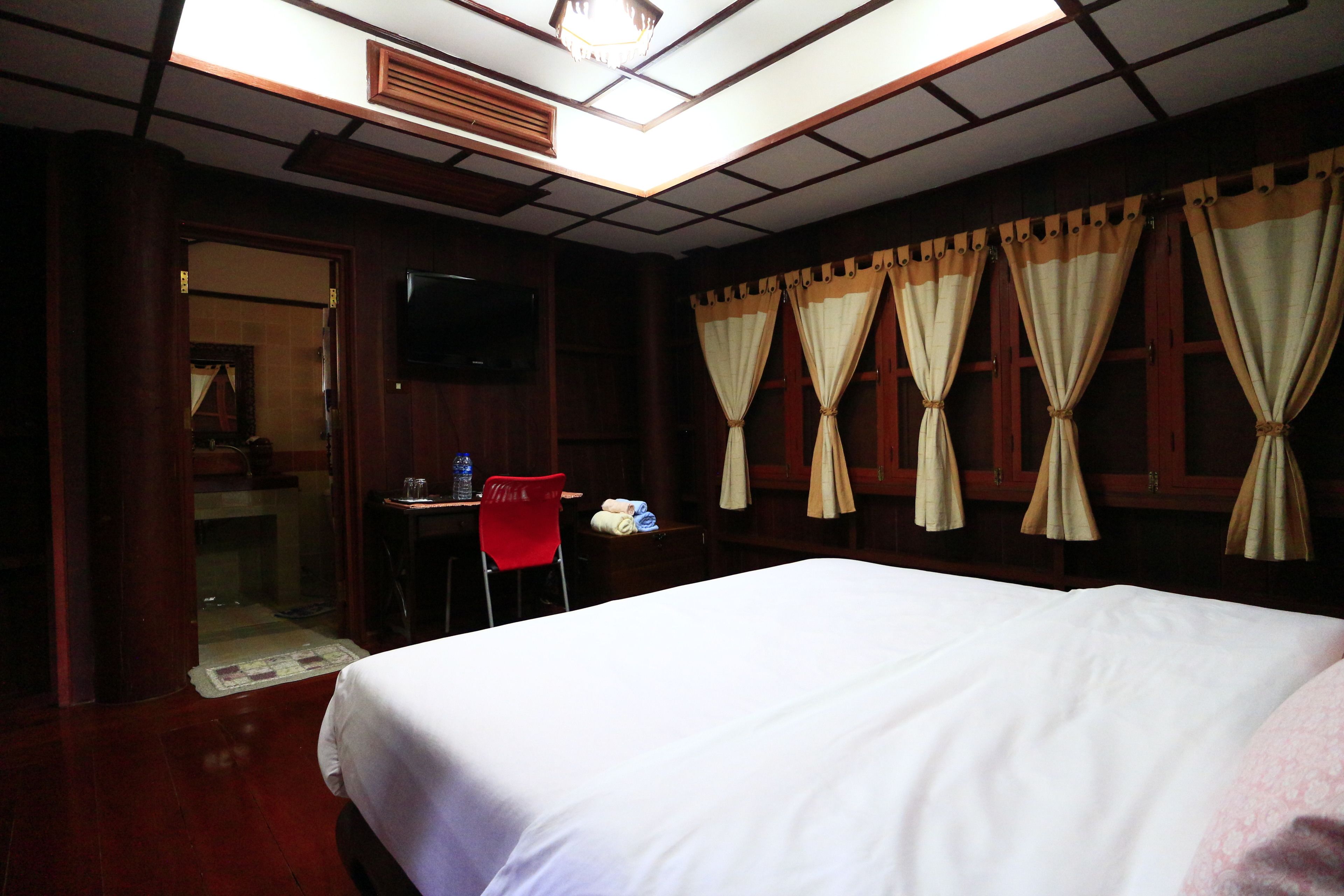Una habitación de hotel con cama, escritorio, silla, televisor y cortinas.