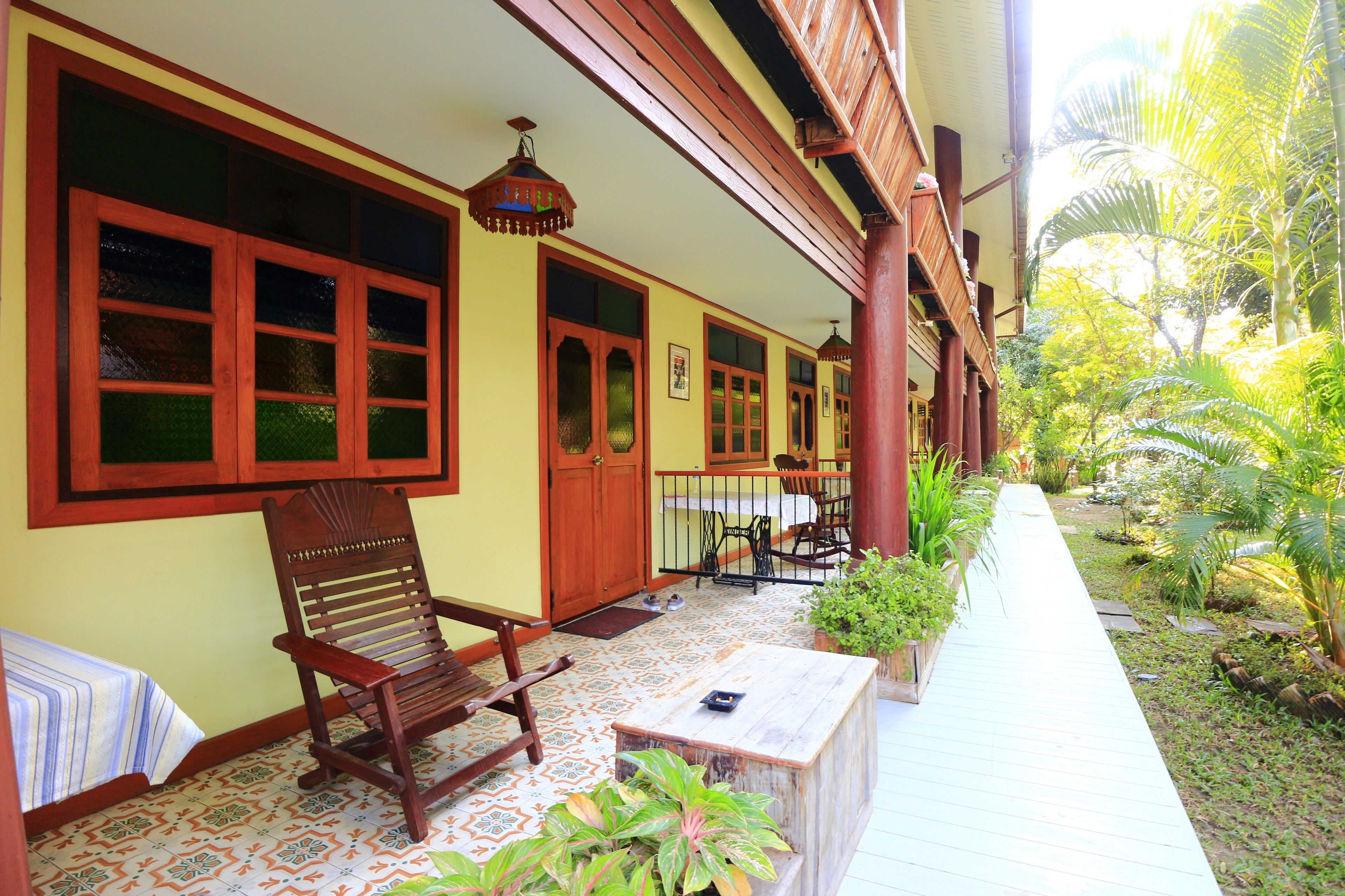 A covered porch with wooden furniture, a tiled floor, and potted plants.
