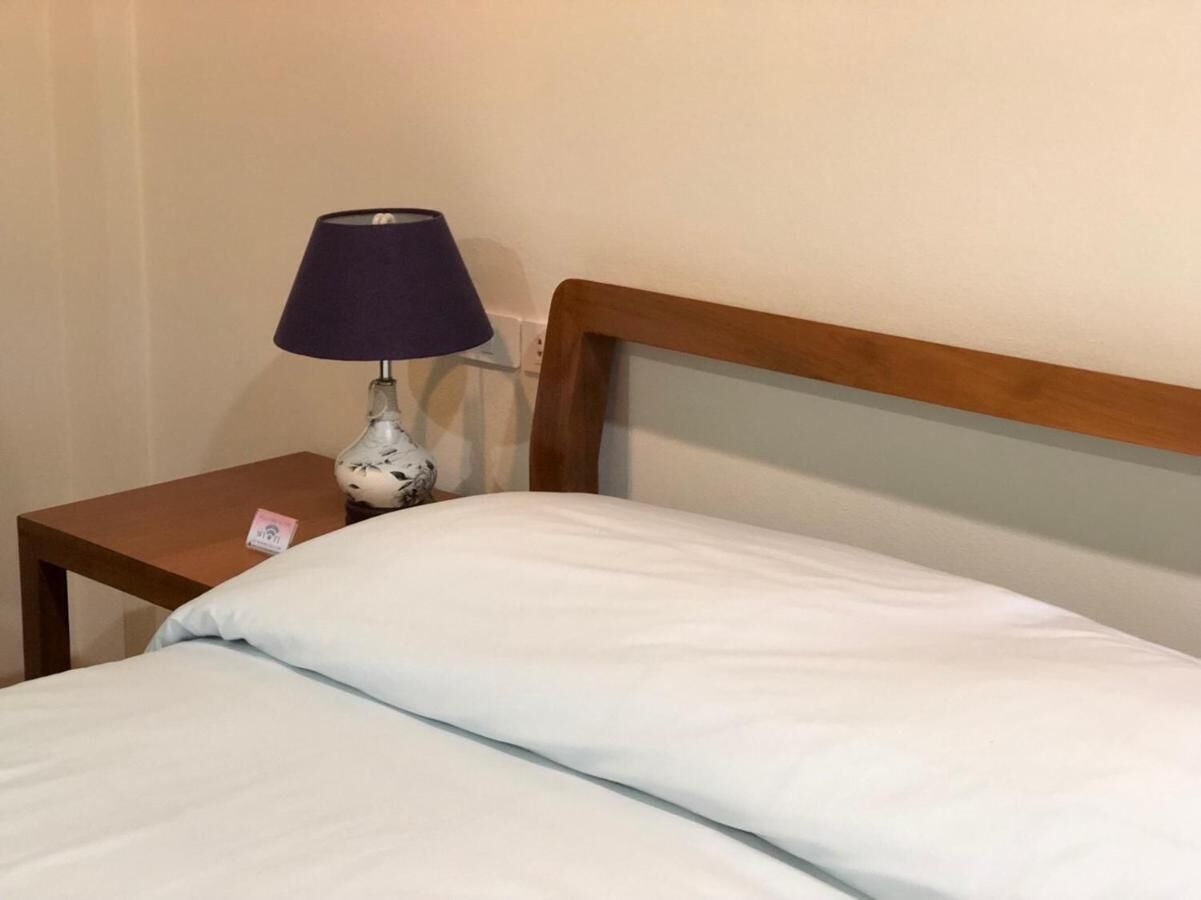 A neatly made bed with a wooden headboard, a small bedside table with a lamp, and a wall socket.