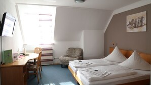 Une chambre d’hôtel équipée d’un bureau, de deux lits, d’une chaise et d’une fenêtre avec des rideaux.