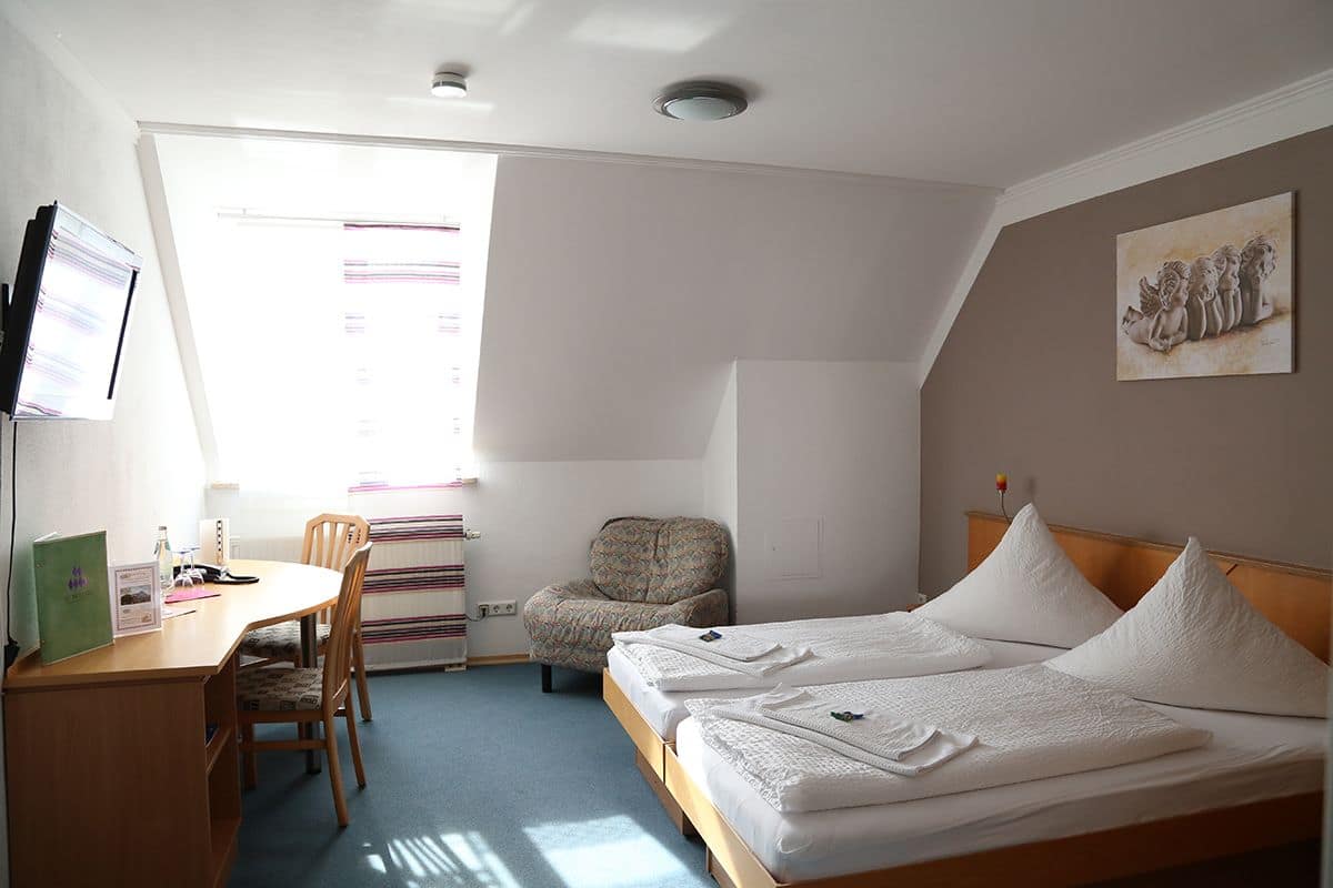 Ein Hotelzimmer mit Schreibtisch, zwei Betten, einem Sessel und einem Fenster mit Vorhängen.