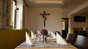A dining table set with wine glasses, napkins, and a centerpiece. A crucifix is mounted on the wall behind the table. - Zu Müllers Winkelhausen (Langenmosen)