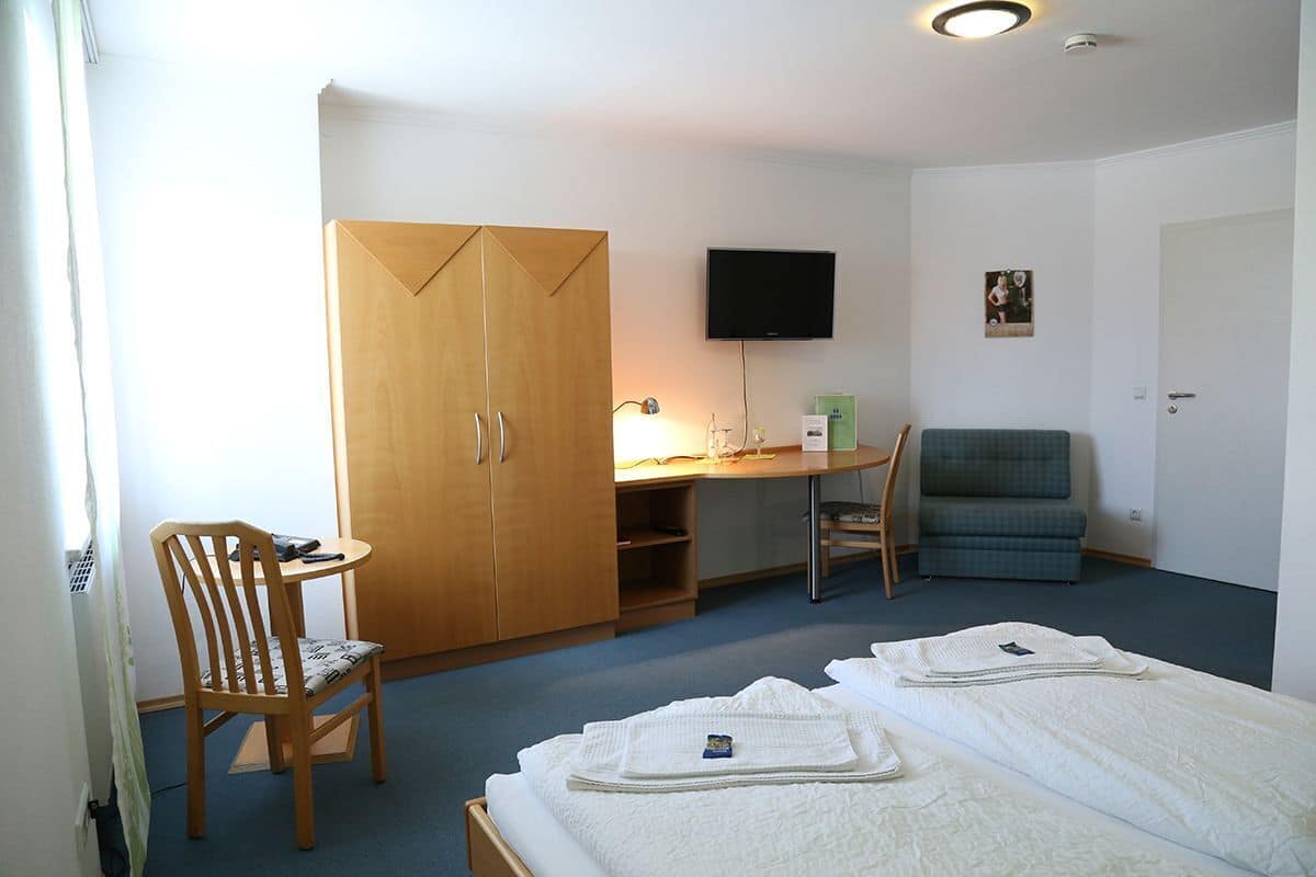 Ein Hotelzimmer mit Bett, Schreibtisch, Stuhl, Kleiderschrank, Fernseher und einem kleinen Bild an der Wand.