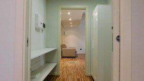 A narrow hallway with a wooden floor, a white bench, a beige chair, and a white refrigerator. - Garden Apartment (Verona)