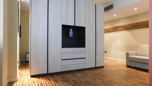 A modern living room with a built-in TV, wooden flooring, and a light-colored sofa. - Garden Apartment (Verona)