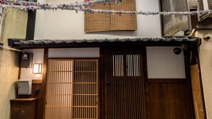A traditional wooden gate with a sliding door, a small step leading up to the entrance, and a wall-mounted light fixture to the left.