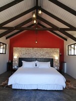 Una cama grande con ropa blanca, una pared de piedra detrás y techo rojo.