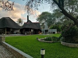 Una cabaña con construcciones de techo de paja, una chimenea central y un césped bien cuidado.