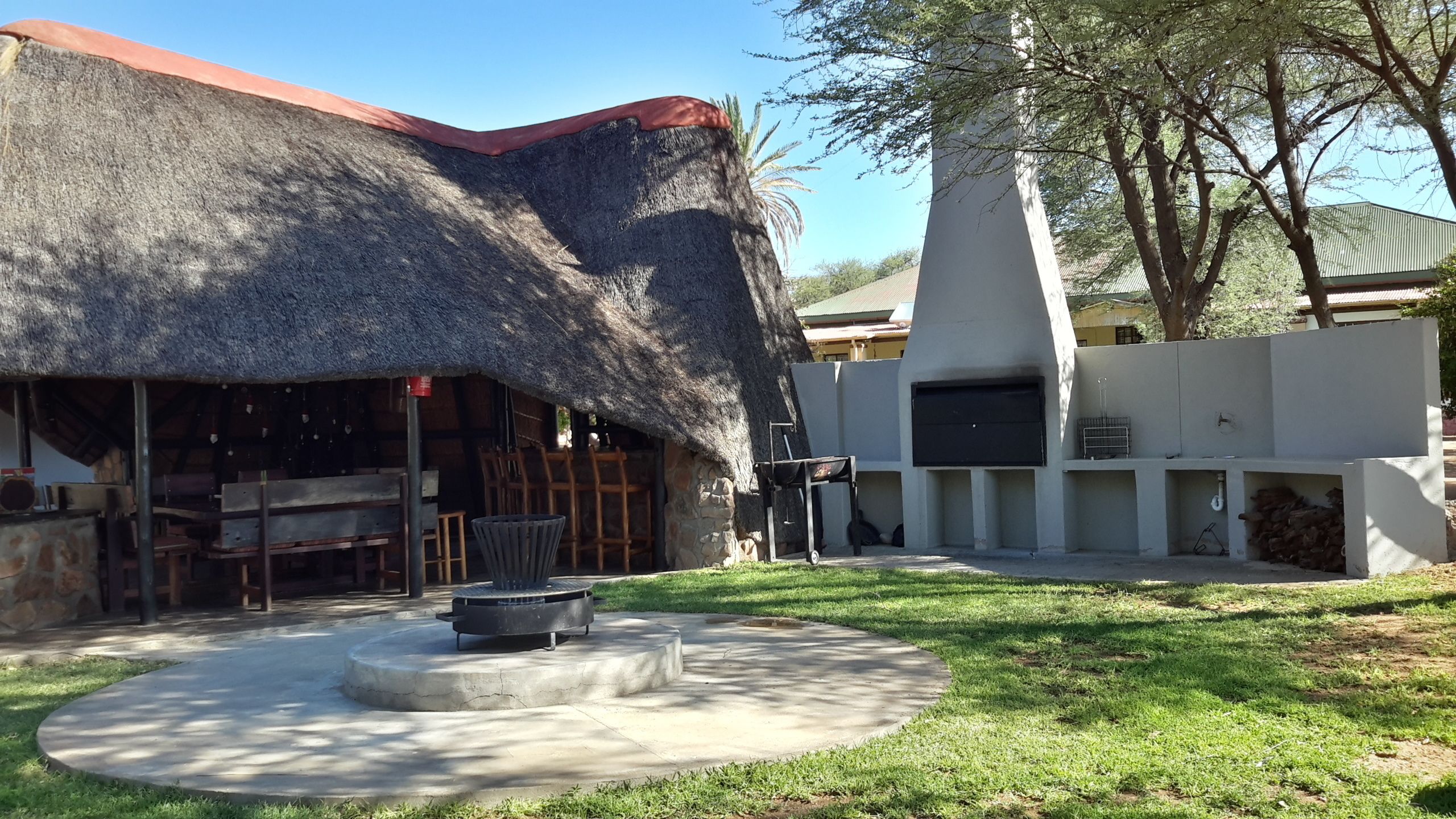 Una construcción con techo de paja, con área de estar al aire libre y parrilla.