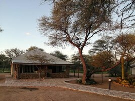 A stone building with a tiled roof, surrounded by a paved area and trees.