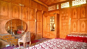 A traditional wooden room with a large bed, a round mirror, and a chair. - De-Laila Houseboats (Srinagar)