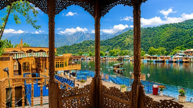 A gazebo with intricate wooden carvings, a view of a river with boats, and a mountainous landscape in the background. - De-Laila Houseboats (Srinagar)