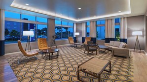 A spacious hotel lobby with a geometric patterned carpet, leather armchairs, a sofa, and a dining table. Large windows offer views of the outside. - TownePlace Suites by Marriott San Diego Airport/Liberty Station (San Diego)