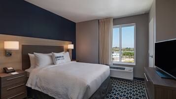 A hotel room with a bed, bedside lamps, a TV, a window with curtains, and a view of the outside.