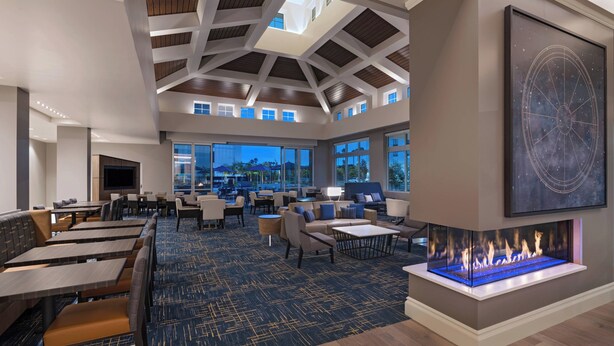 A spacious lounge area with a high ceiling, a fireplace, and large windows offering a view of the outdoors. - TownePlace Suites by Marriott San Diego Airport/Liberty Station (San Diego)