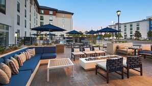 An outdoor seating area with sofas, chairs, and umbrellas, surrounded by buildings. - TownePlace Suites by Marriott San Diego Airport/Liberty Station (San Diego)