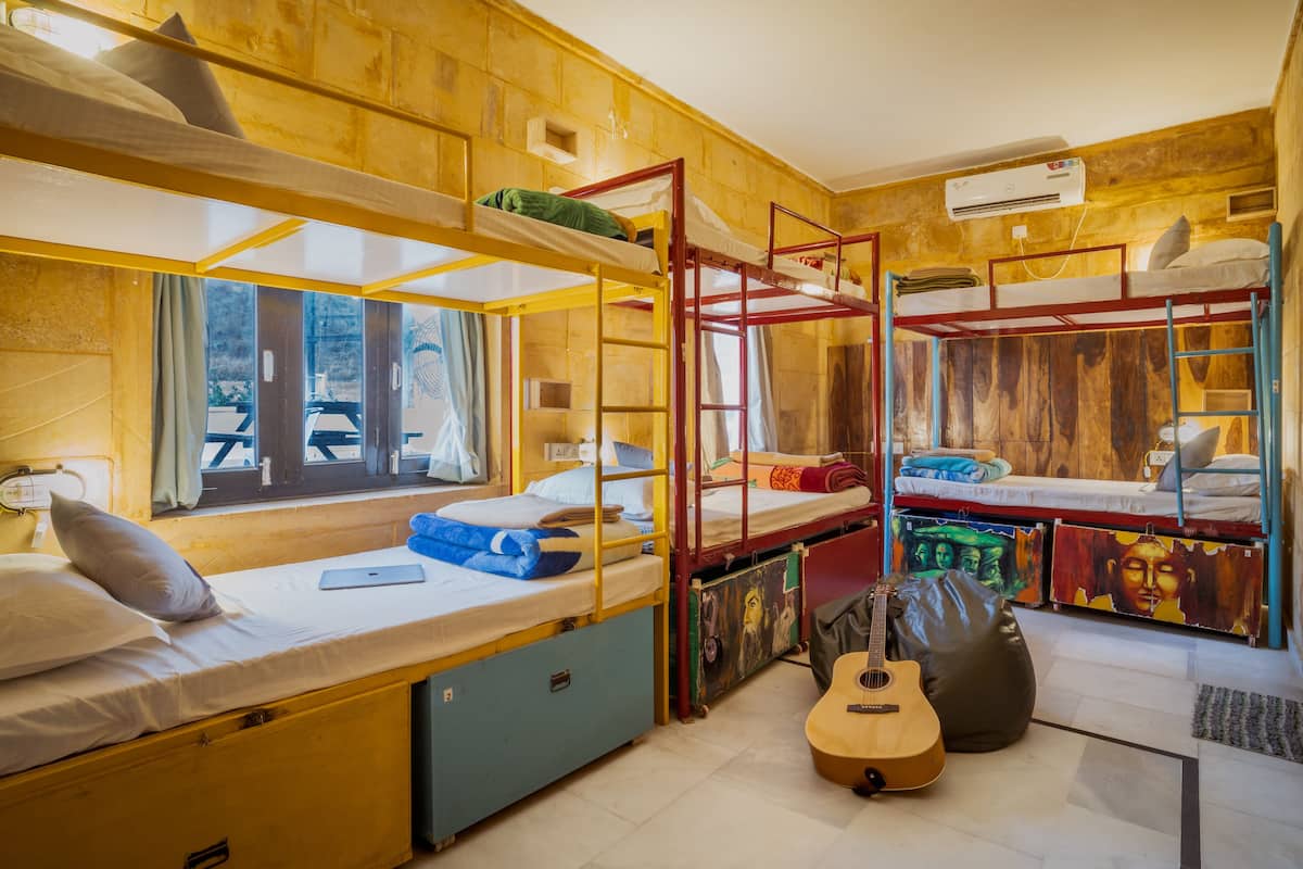 Quarto estilo dormitório com beliches, um violão e uma janela com vista.
