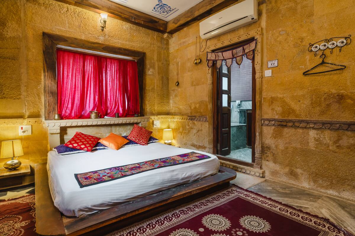 Quarto tradicional com cama, cortinas vermelhas e vista para o exterior.