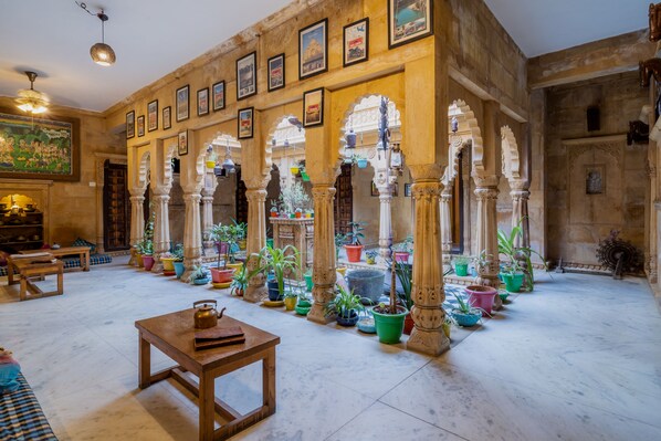 A spacious room with a high ceiling, ornate arches, and a variety of potted plants.